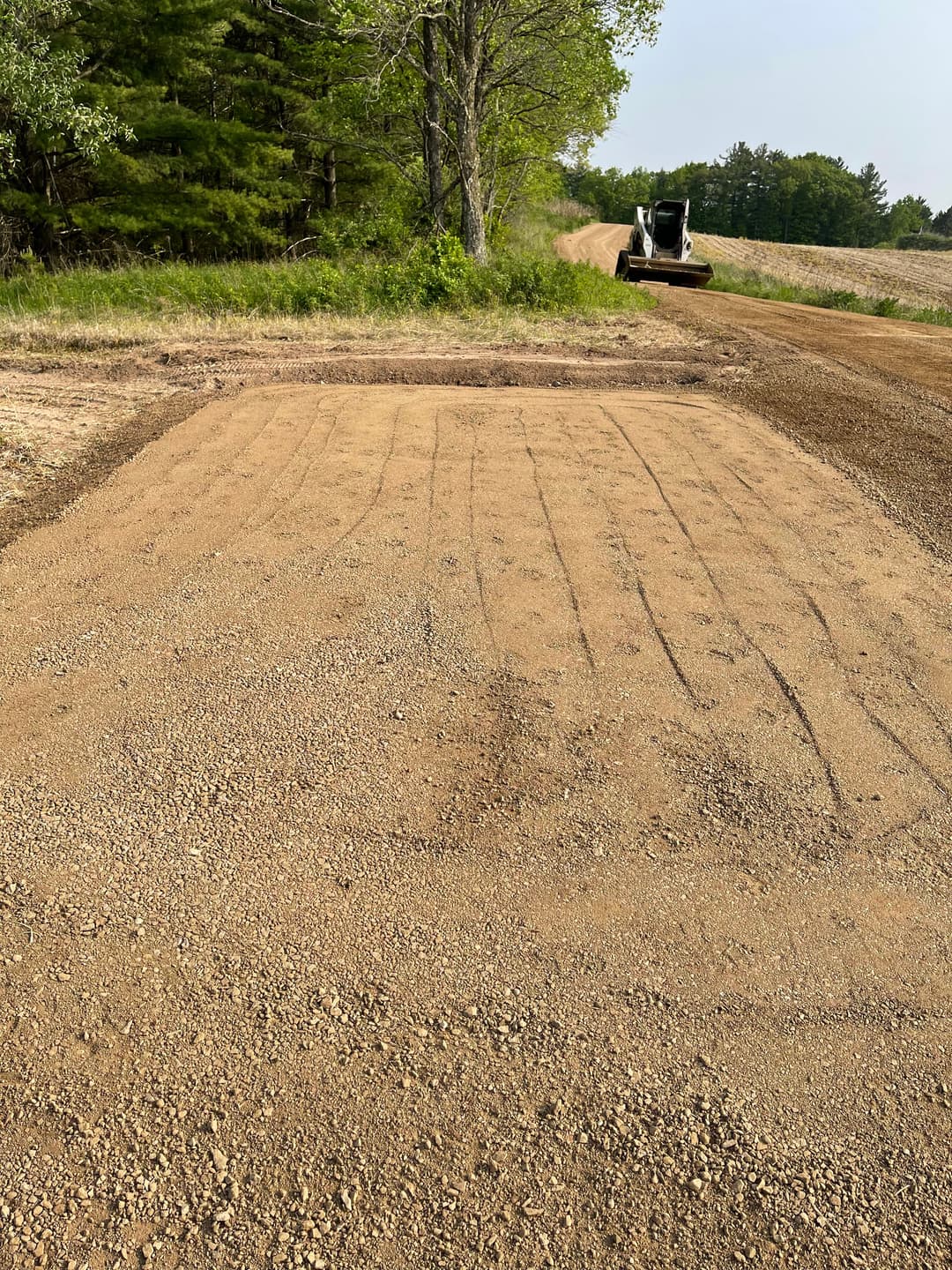 Cleared and graded dirt area with machinery in the background on rural landscape.